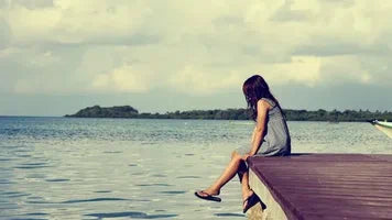 A woman sitting at the edge of a dock and looking across the water