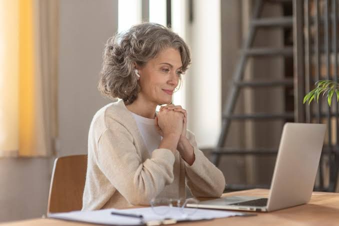 An older woman sitting at a table and watching a laptop
